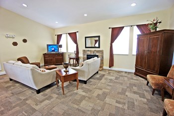 Interior of the clubhouse with carpeted flooring, beige couches, brown chest and wardrobe and end table, tv, and fireplace
